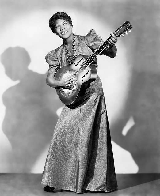 Black and white photo of Black woman in dress standing with guitar looking up smiling