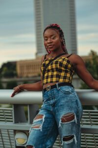Black Alt Women posing and smiling confidently with pink braids, yellow plaid top and ripped jeans. Maybe she downloaded her Free Survivor Resource Guide!